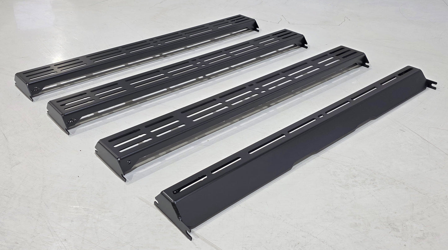 Four Wide Ruggedized Crossbar Kits for the 5th Gen 4Runner are arranged parallel to each other on a white floor, viewed from above. The crossbars are sturdy and black, designed for optimal functionality and style.