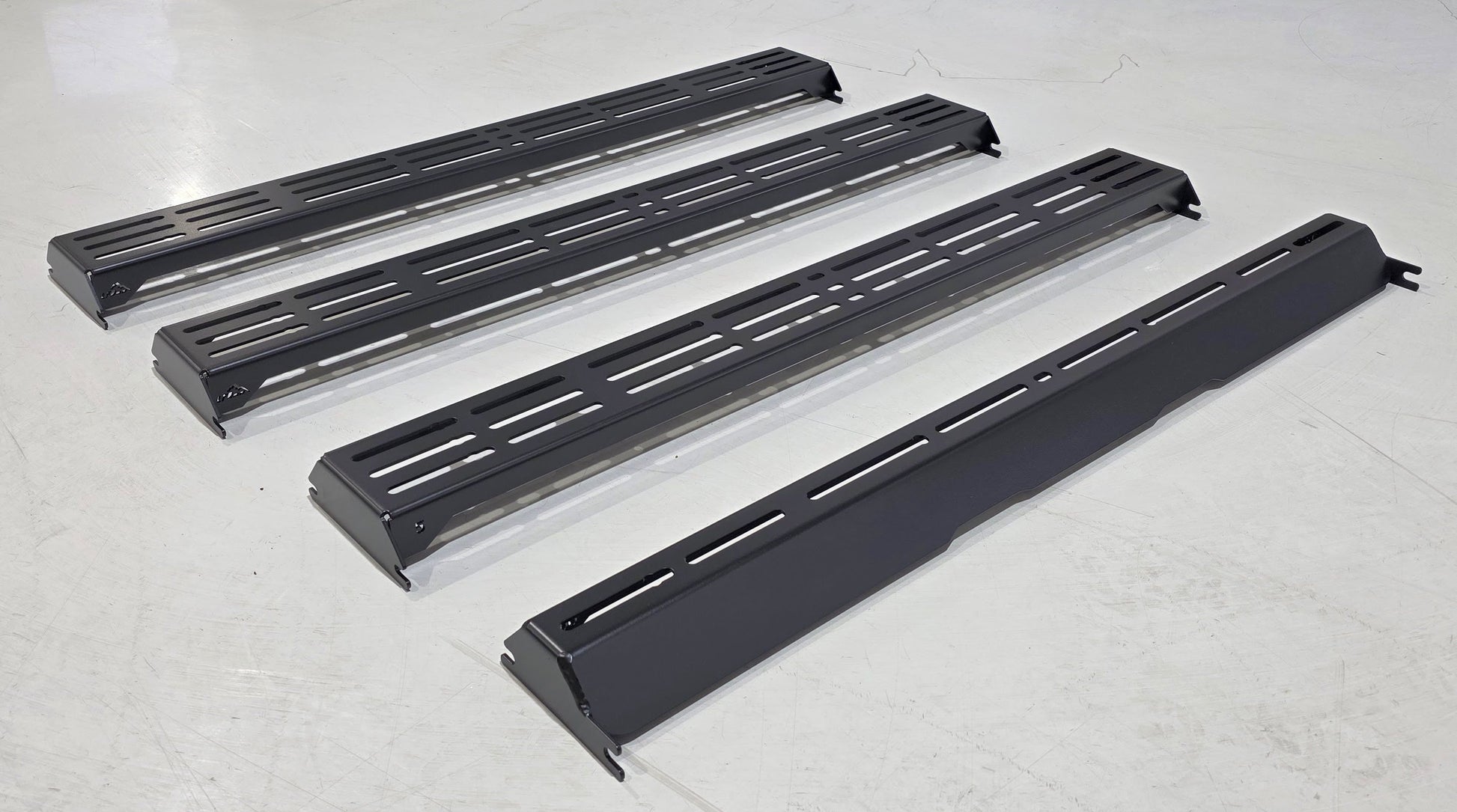 Four Wide Ruggedized Crossbar Kits for the 5th Gen 4Runner are arranged parallel to each other on a white floor, viewed from above. The crossbars are sturdy and black, designed for optimal functionality and style.