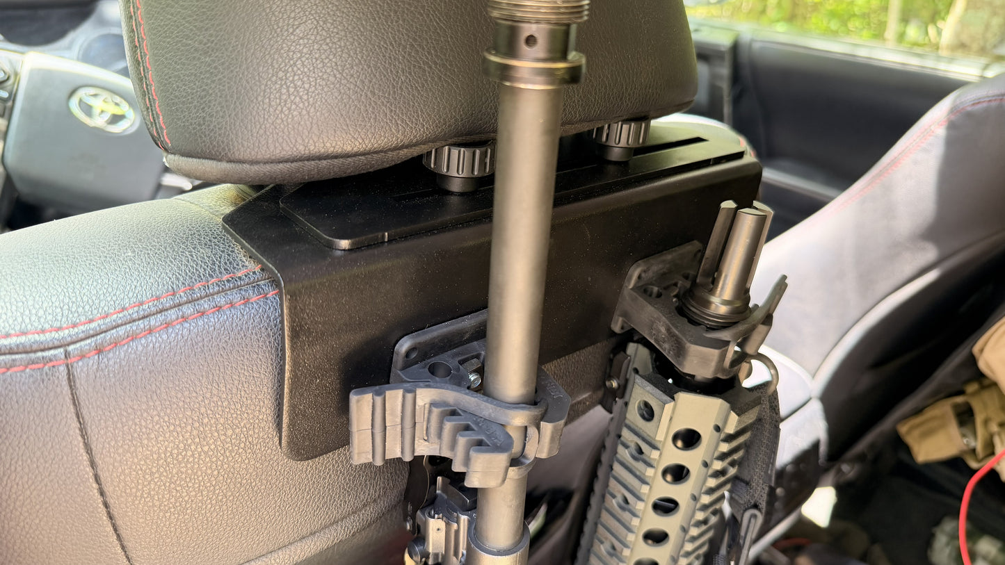 Two rifles secured in a Headrest Rifle Mount - HRM attached to the back of a car seat, with part of the vehicle's interior visible.