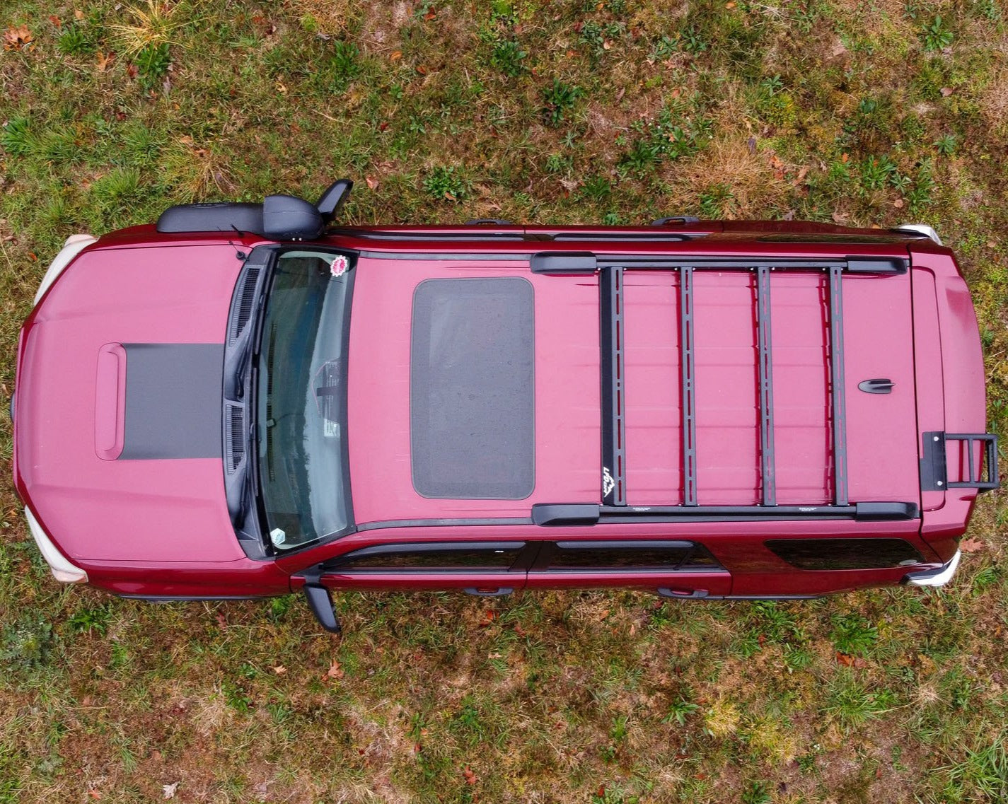 Aerial view of a red 5th Gen 4Runner with a Ruggedized Crossbar Kit - 5th Gen 4Runner parked on patchy green and brown grass, highlighting the sturdy roof storage solution mounted on top.