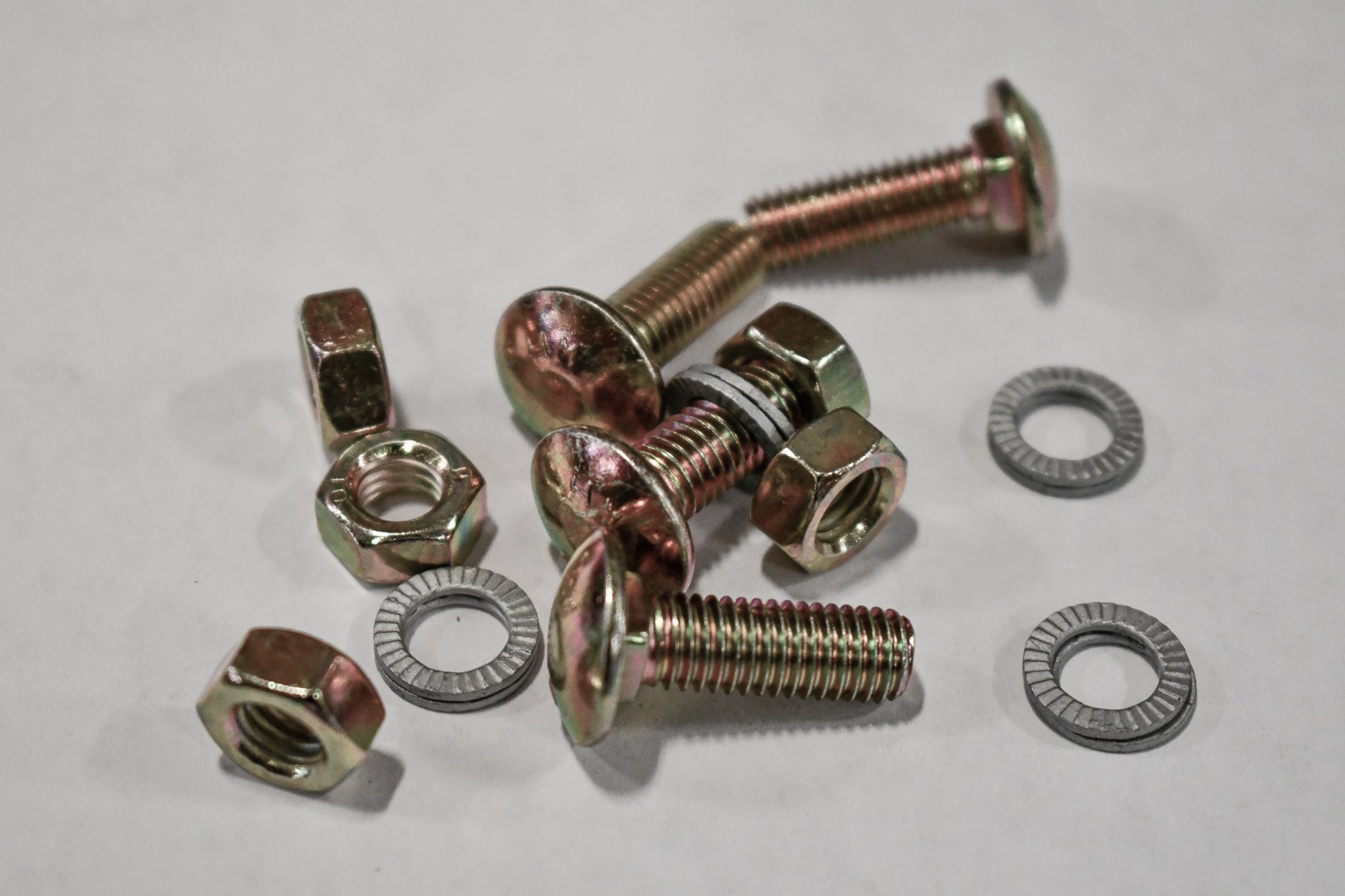 Several metallic bolts, nuts, and golden-hued washers—perfect for 3/4 Roof Rack - 5th Gen 4Runner installation—are scattered on a light gray surface. The rugged washers fit crossbars or roof rack accessories.