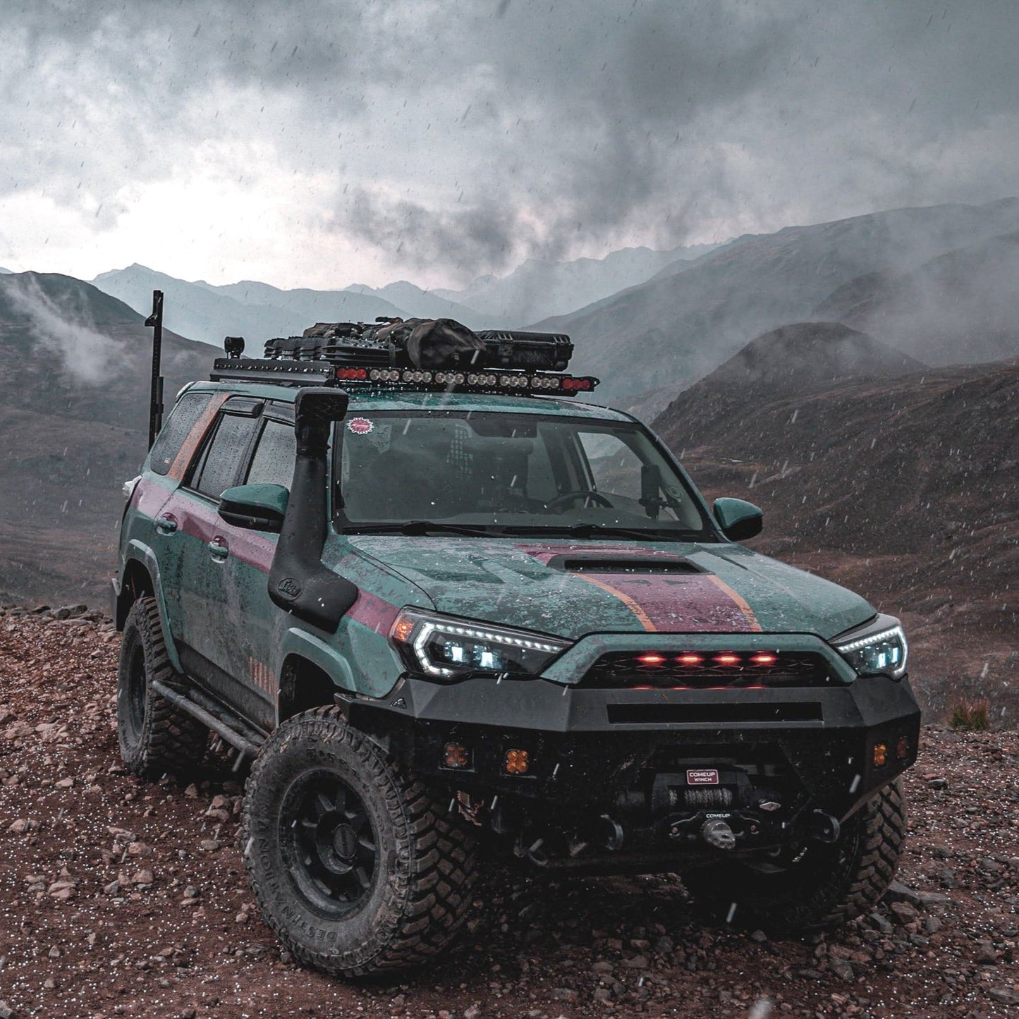 A rugged 5th Gen 4Runner SUV with large tires and a 7/8 Roof Rack - 5th Gen 4Runner is parked on rocky terrain beneath an overcast sky, mountains towering in the background.