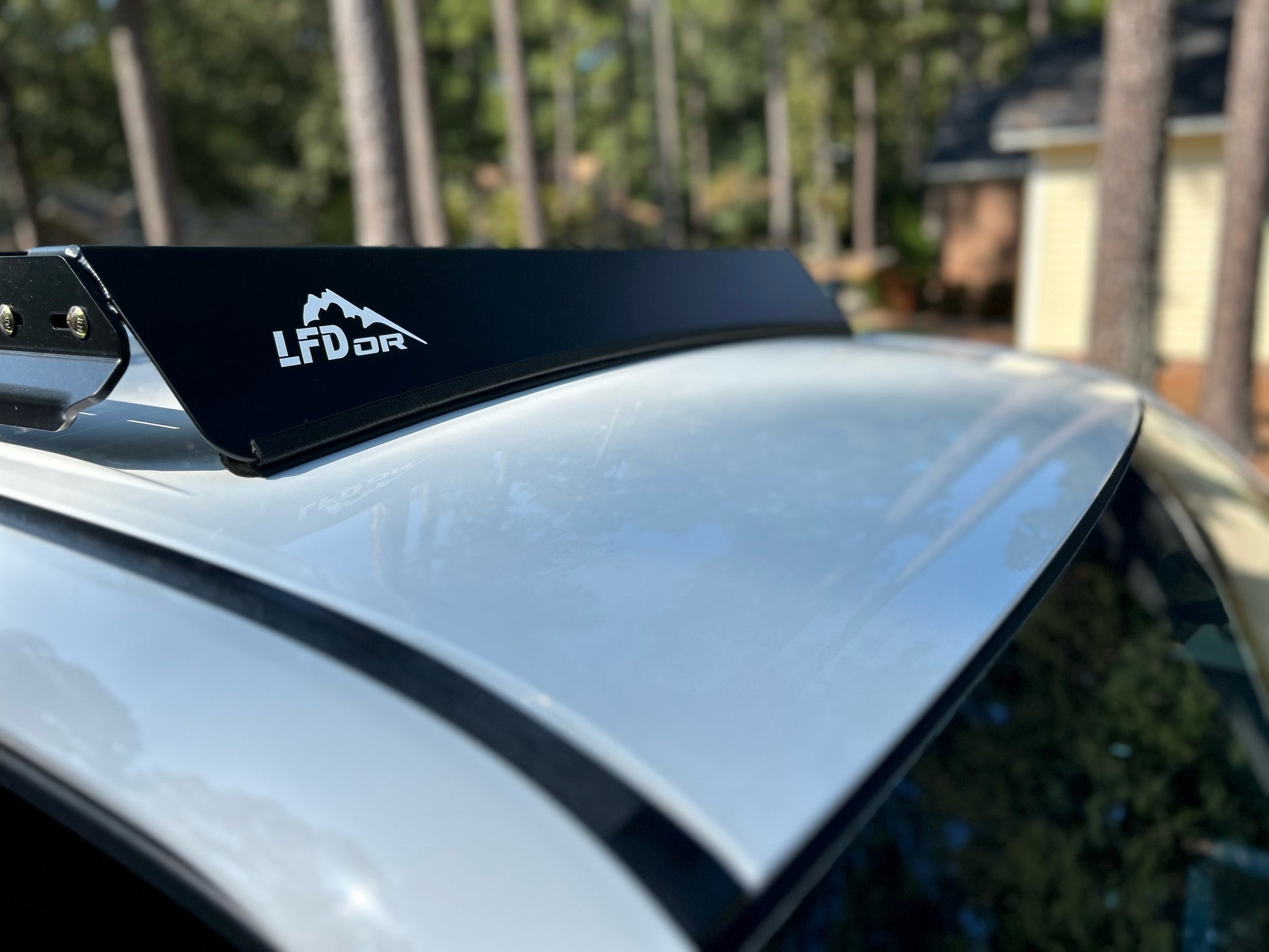Close-up of a white 5th Gen 4Runner’s roof equipped with the black 7/8 Roof Rack; ruggedized crossbars are in focus, with trees and a blurred house in the background.