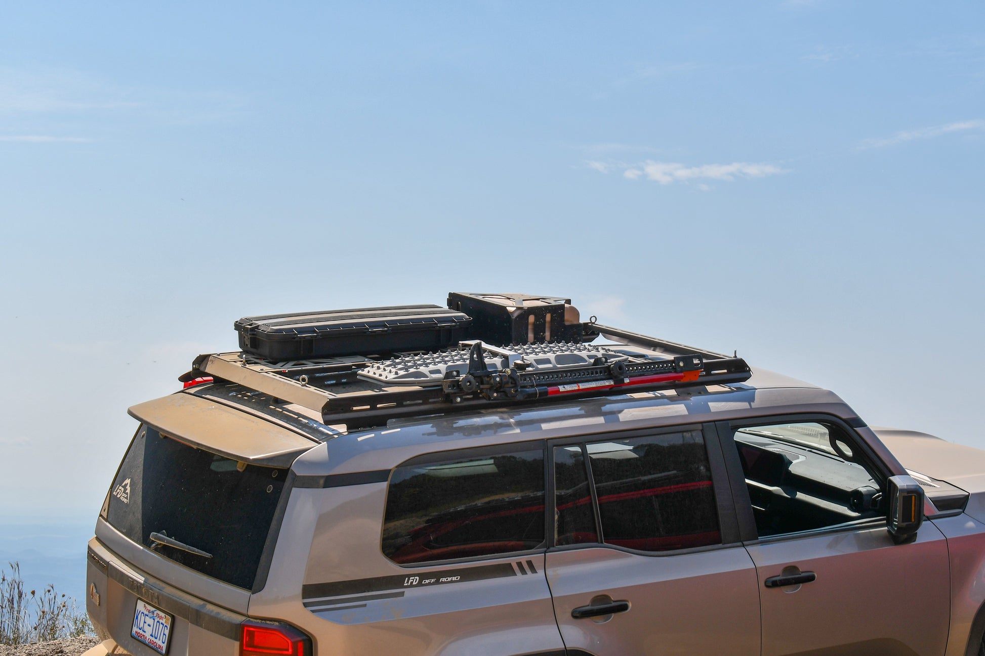 A gray SUV with a 7/8 Roof Rack - 250 Series Land Cruiser (2024+) is parked outdoors, loaded with storage cases and gear, set against a scenic sky and distant landscape.